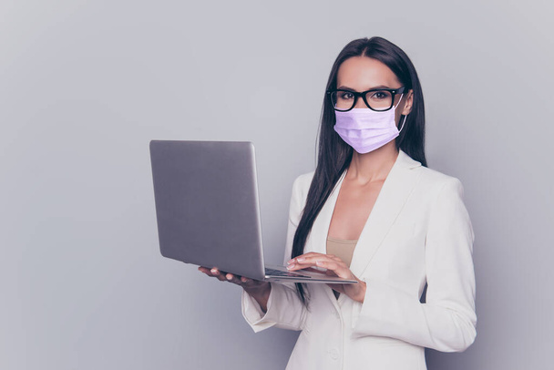 Portrait of business lady in violet face mask holding laptop in hands isolated on grey colored background - Fotografie, Obrázek