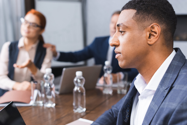 Бічний погляд на афроамериканського бізнесмена біля розмитих колег на задньому плані в залі засідань - Фото, зображення