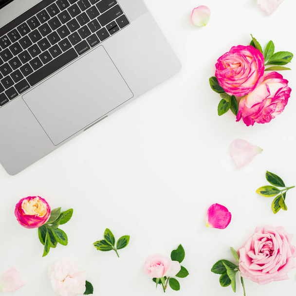 Laptop met roze rozen bloemen en bloemblaadjes op witte achtergrond. Plat gelegd. Bovenaanzicht. - Foto, afbeelding