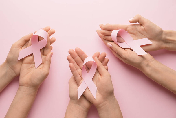 Female hands with pink ribbons on color background. Breast cancer awareness concept - Zdjęcie, obraz