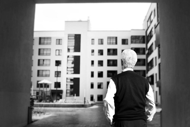 Egy idős férfi egy építkezést néz otthon. A kilátás hátulról. Fekete-fehér. - Fotó, kép