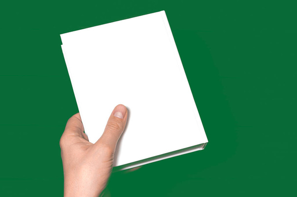 Een mock-up van een wit gesloten boek met een plaats voor tekst in de hand van een man - Foto, afbeelding