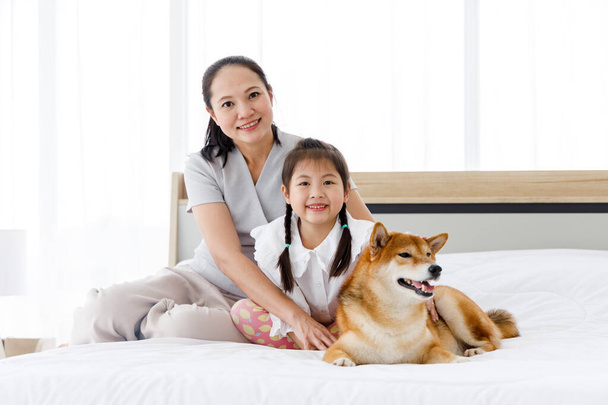 Asian mother and daughter sitting on the bed with Shiba Inu lying on the right side. Concept family with dog at home. - Photo, Image