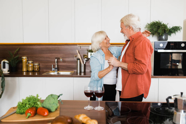 Szczęśliwa wesoła para seniorów tańczy w kuchni świętują rocznicę lub urodziny - Zdjęcie, obraz