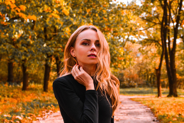 Portret van een jonge vrouw met blond haar in het gouden park. Herfstconcept. Vallende bladeren - Foto, afbeelding