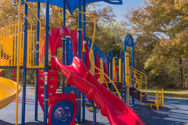Close-up red slide tube of vibrant playground with colorful fall foliage in Flower Mound, Texas, America. Public playground with shade sail and rubber mat flooring near nature park - Photo, Image