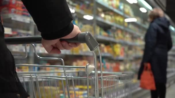 CHOOSE PRODUCTS ON THE SUPERMARKET. SLOW MOTION. A look next to a moving empty cart in a store. Human hand. Close-up - Video