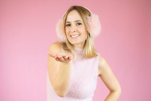 Portrait of a lovely young woman in pink earmuffs sending kiss isolated over pink background - Fotó, kép