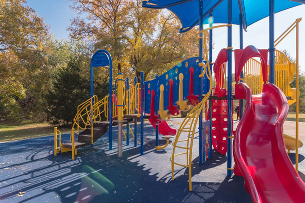 Close-up red slide tube of vibrant playground with colorful fall foliage in Flower Mound, Texas, America. Public playground with shade sail and rubber mat flooring near nature park - Photo, Image