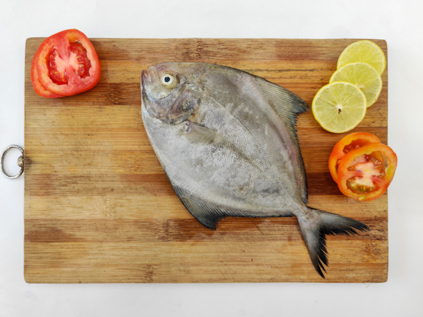 Lähikuva näkymä musta Pomfret kala koristeltu vihanneksia ja yrttejä puinen tyyny, valkoinen tausta. - Valokuva, kuva