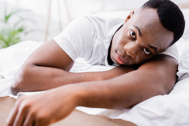 African american man in white t-shirt looking at camera on bed  - Foto, Bild