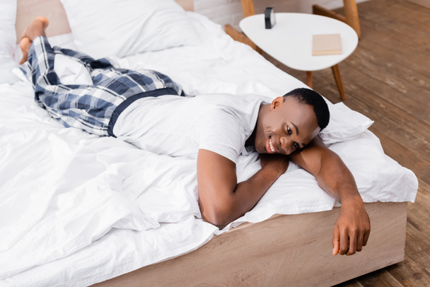 Smiling african american man in pajamas lying on bed during morning  - Fotografie, Obrázek