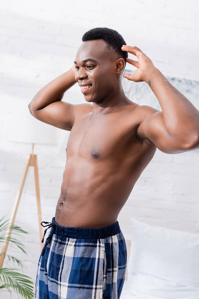 Shirtless african american man smiling while stretching at home during morning  - Fotografie, Obrázek