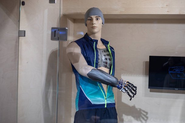 Foto een etalagepop in de vorm van een jonge man in sportkleding met een prothetische arm achter glas. Demonstratie van nieuwe technologieën in protheses. Een robothand. Prothese concept. - Foto, afbeelding