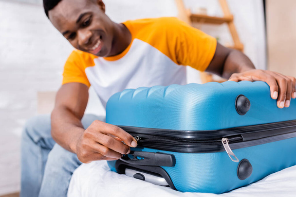 African american man locking suitcase on bed on blurred background  - Zdjęcie, obraz