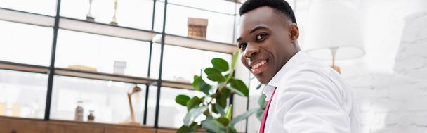 Vista lateral del hombre de negocios afroamericano sonriendo a la cámara en casa, pancarta  - Foto, Imagen