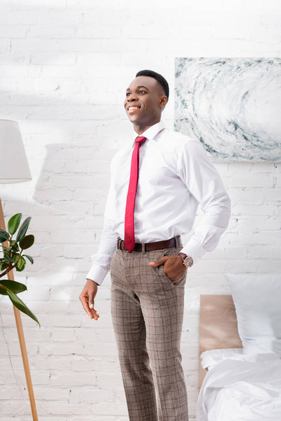Mosolygó afro-amerikai üzletember áll az ágy mellett otthon  - Fotó, kép