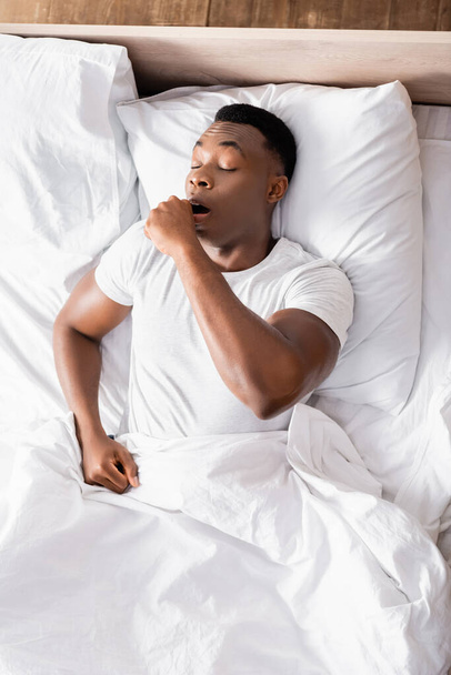 Вид на африканского американца зевающего на кровати  - Фото, изображение