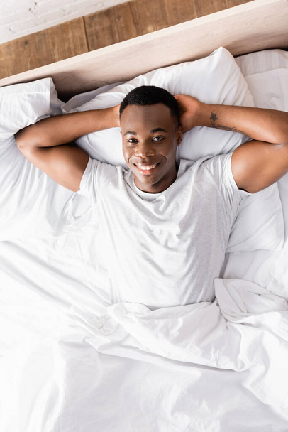 Top view of tattooed african american man smiling at camera on bed  - Photo, image