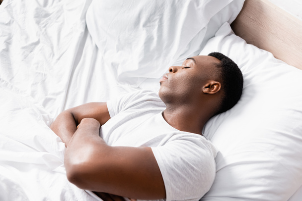 Vista de alto ángulo del hombre afroamericano con brazos cruzados durmiendo en la cama por la mañana  - Foto, imagen