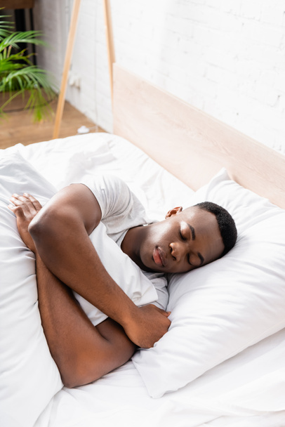 African american man embracing blanket while sleeping on bed at home  - Foto, Imagen