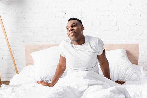 Smiling african american man sitting on bed at morning  - Фото, изображение