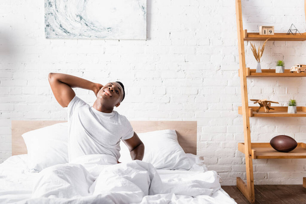 Cheerful african american man stretching on bed at morning  - Foto, afbeelding