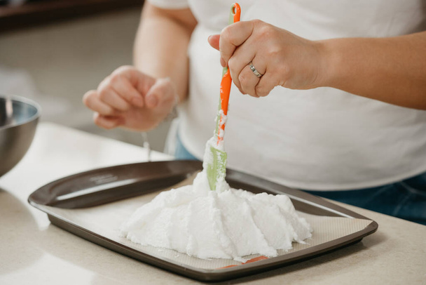Photo des mains d'une jeune femme qui améliore avec une omoplate la forme d'une meringue géante sur un plateau. Une fille se prépare à cuisiner une délicieuse tarte à la meringue au citron. - Photo, image
