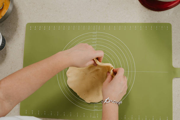 Una foto cercana de las manos de una joven que está desplegando masa de pan corto en la cocina - Foto, imagen