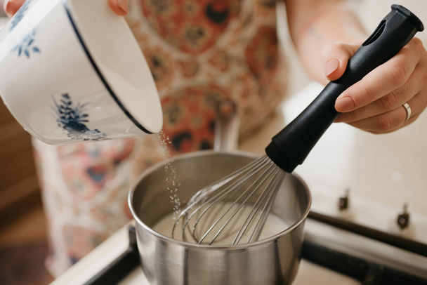 カローラクリームで混合している若い女性の手の近くの写真,砕いたゼスト,レモン汁とガスストーブの上の鍋に砂糖を追加 - 写真・画像