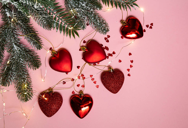 Arbre de Noël avec des jouets rouges, des cœurs et une guirlande lumineuse sur fond rose - Photo, image