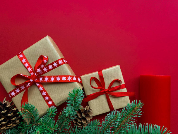 Kerst achtergrond. Cadeaudoosjes met ambachtelijk papier en rode strikken, sparren takken en rode kaars. Bovenaanzicht met kopieerruimte. - Foto, afbeelding