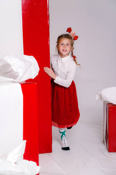 niña divertida feliz en traje de Navidad con grandes regalos rojos en el fondo. - Foto, Imagen