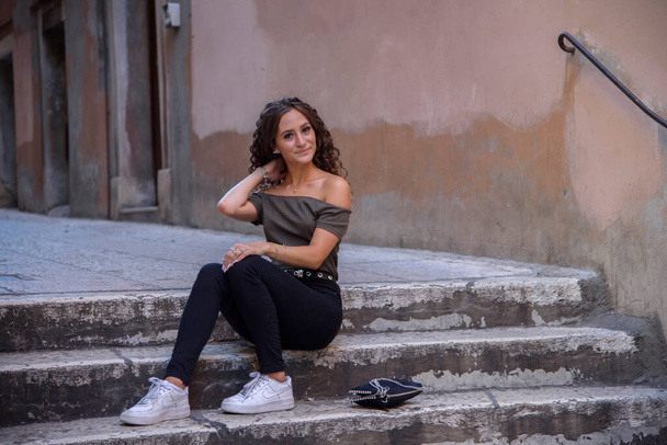 Young curly girl sitting on a stair in a city during the day. - Fotografie, Obrázek