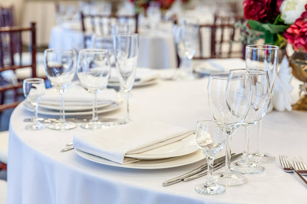 Fantazyjny zestaw stołowy do kolacji z serwetkami w restauracji, luksusowe tło wnętrza. Wedding eleganckie dekoracje bankietowe i przedmioty do żywności zorganizowane przez obsługę cateringową na białym stole obrus - Zdjęcie, obraz