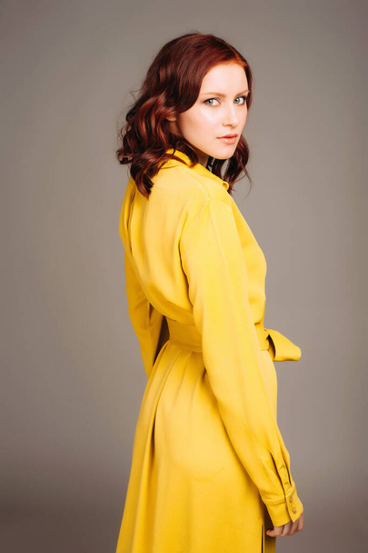 Fiatal vörös nő sárga ingben. Női ragyogó megjelenés, citromos alkalmi stílus. Divatportré semleges stúdióháttérrel. - Fotó, kép