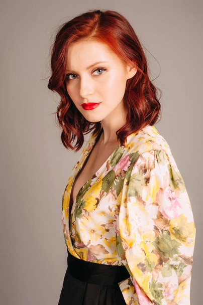 Female fashion. Redhead model in evening dress with long yellow balloon sleeves posing on grey studio background. Young woman with red lips and natural hairdo. Fashion concept. - Photo, Image