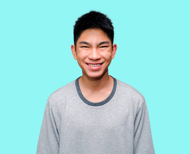 Egy ragyogó, mosolygós ázsiai fiatalember boldognak tűnik egy elbűvölő kifejezéssel, és a kék háttér sokkolja. Vidám férfiak szürke póló mockup kék háttér modell. vágási útvonallal. - Fotó, kép