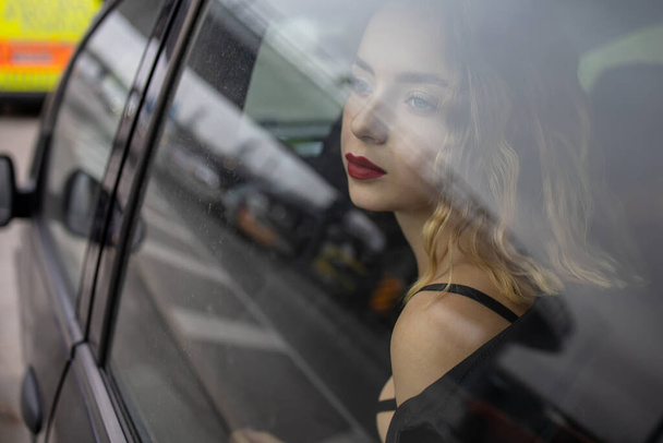 赤い唇を持つ美しいファッション女性が車の中で座っています. - 写真・画像