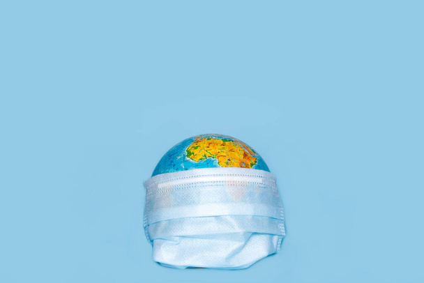 COVID-19 conceito de vírus com globo em máscara cirúrgica no fundo azul com lugar para texto e espaço de cópia. - Foto, Imagem