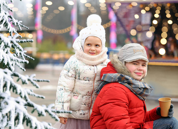 Κορίτσι με λευκό καπέλο και σακάκι και αγόρι με κόκκινο παλτό και καπέλο. Αδελφός και αδελφή διασκεδάζουν στο δρόμο το χειμώνα. Χριστουγεννιάτικες διακοπές. Νέο έτος. - Φωτογραφία, εικόνα