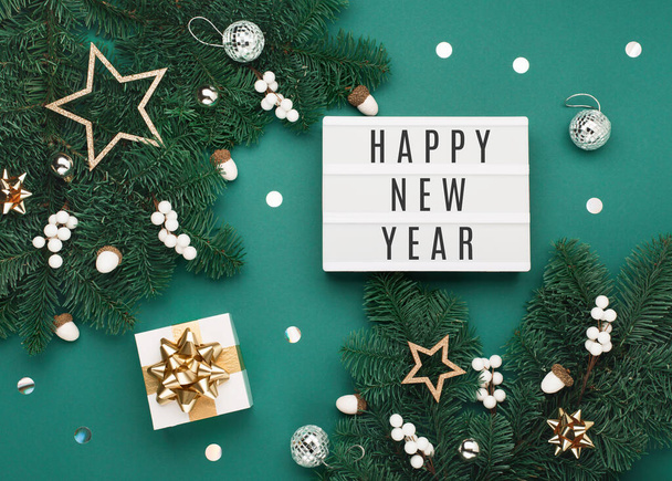 Happy New Year tekst op witte Lightbox met geschenkdoos, vakantie zilver en gouden decoraties, eikels op groene kerstboom takken achtergrond. Platte lay, bovenaanzicht, kopieerruimte. Feestelijke wintertijd. - Foto, afbeelding