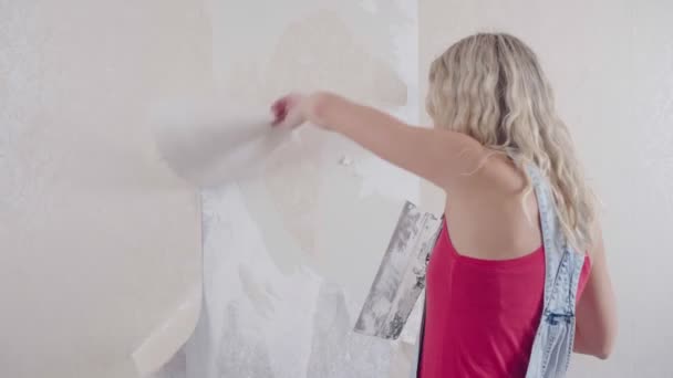 Une femme arrache le vieux papier peint du mur et fait des réparations dans la maison - Séquence, vidéo