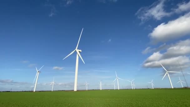 Parc d'hélices d'éoliennes qui produisent de l'électricité. Moulin à vent Production de technologies éoliennes Hélice de parc éolien debout sur un champ en pleine floraison dans un champ vert avec ciel bleu, production d'énergie renouvelable durable - Séquence, vidéo