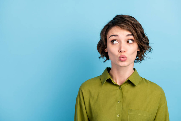 Photo portrait of pretty young shy girl looking at side sending air kiss with plump pouted lips wearing green shirt isolated on blue color background with blank space - Φωτογραφία, εικόνα