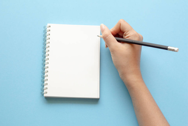 mulher mãos escrevendo em caderno vazio na mesa azul. Flat lay vista superior. - Foto, Imagem