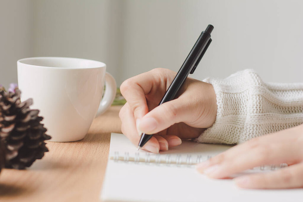 Mujer con un suéter acogedor escrito en el cuaderno con una taza de café en el escritorio. Otoño e invierno. - Foto, imagen