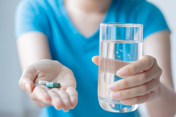 Οι γυναίκες παίρνουν φάρμακα και κρατούν ένα ποτήρι καθαρό νερό. έννοια της υγειονομικής περίθαλψης. - Φωτογραφία, εικόνα