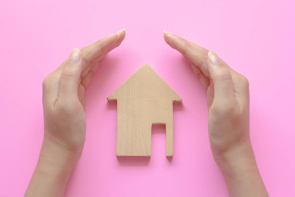 Modelo de casa de madera en manos de mujer sobre fondo rosa. Ofertas hipotecarias, atención domiciliaria y concepto de seguro de vivienda familiar. - Foto, imagen