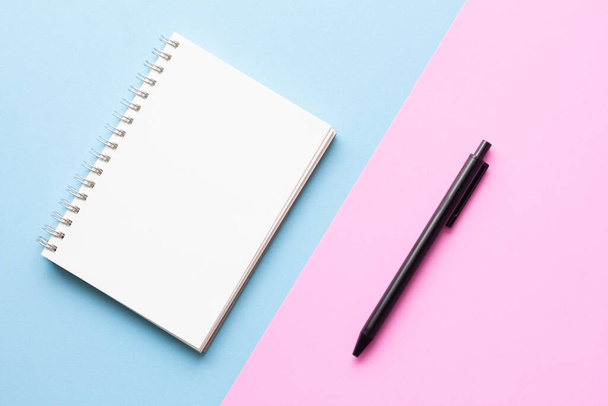 Pose plate de bloc-notes avec stylo sur fond bleu pastel et rose, style minimal. Espace de travail duo ton. - Photo, image